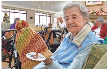 senior woman holds up a hat she knitted at a senior living community