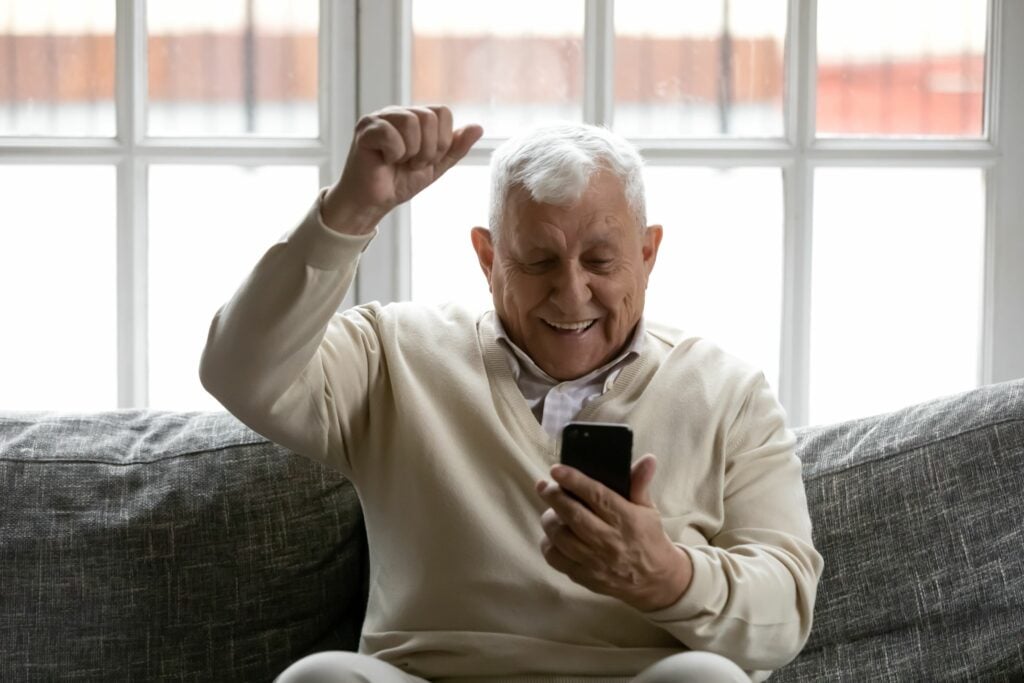 senior man is happy and excited while looking at his cellphone on a couch