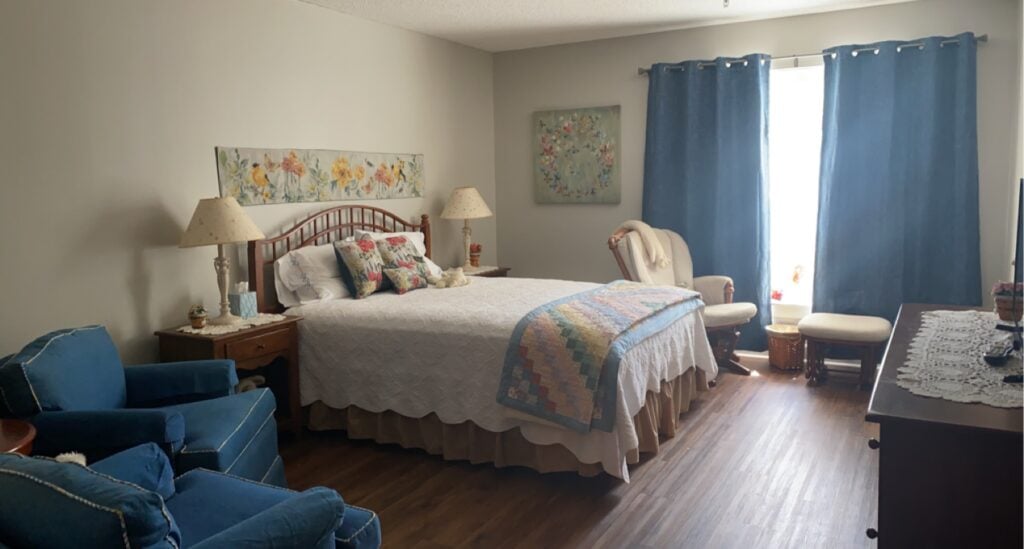 senior apartment bedroom with a large bed, three chairs, a dresser and wide window