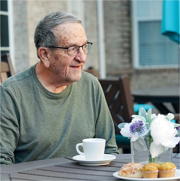 A senior man smiles while sitting outside on a patio at a senior living community