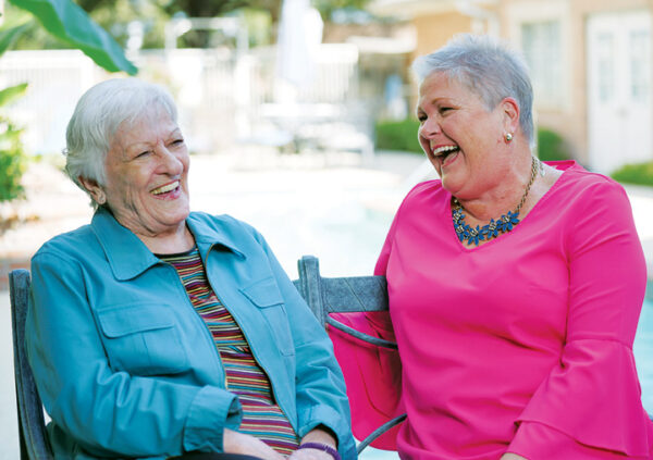 A female team member and senior woman smile while sitting outside at a senior living community