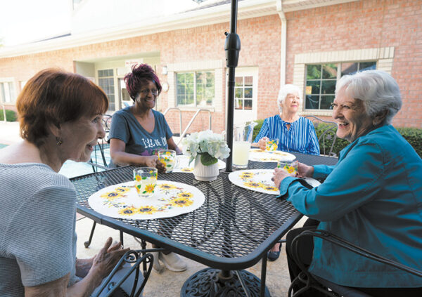 Four senior women enjoy lemonade together outside at a senior living community