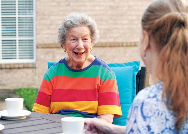 Smiling residents sharing a cup of coffee in the outdoor courtyard of a Sonida Senior Living assisted and independent living community.