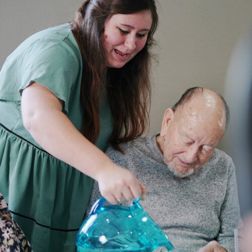 woman activity director pours water into a jar for a senior man resident