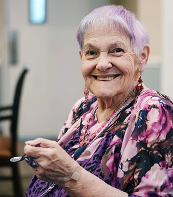 senior woman smiles while eating ice cream in the dining room