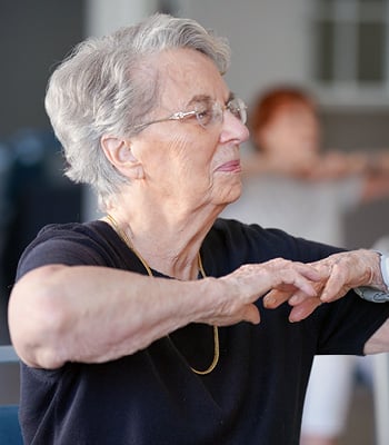 senior woman smiles while doing a stretching exercise in a senior living community