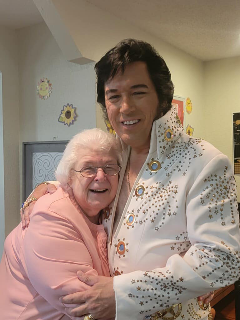 Senior woman smiles while hugging an Elvis impersonator at Riverbend, a senior living community