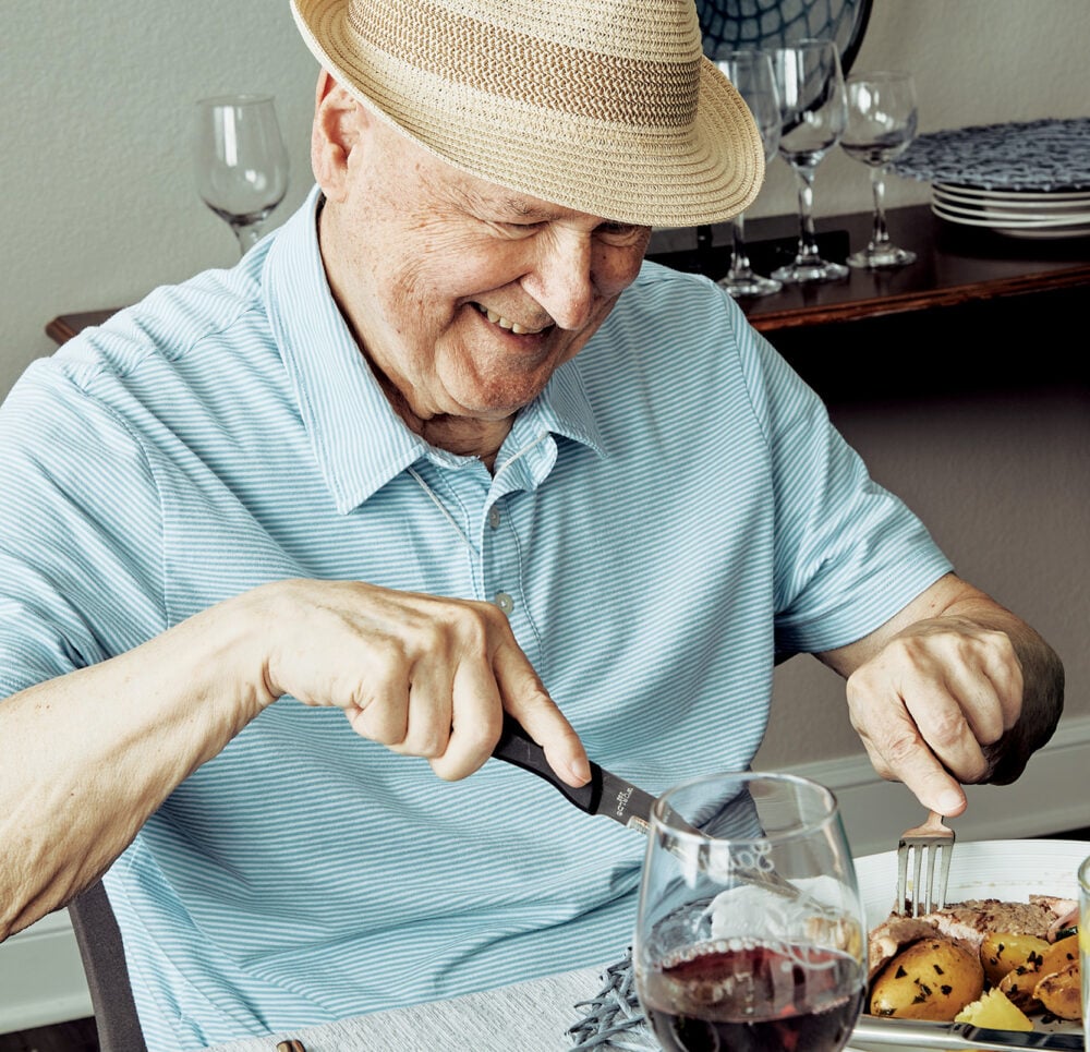 Senior man smiles while cutting into a piece of meat at a dining table