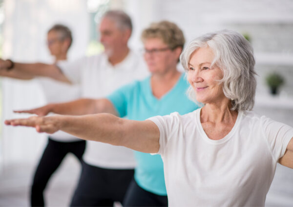 A multi-ethnic group of adult men and women are indoors in a fitness studio participating in a yoga class.