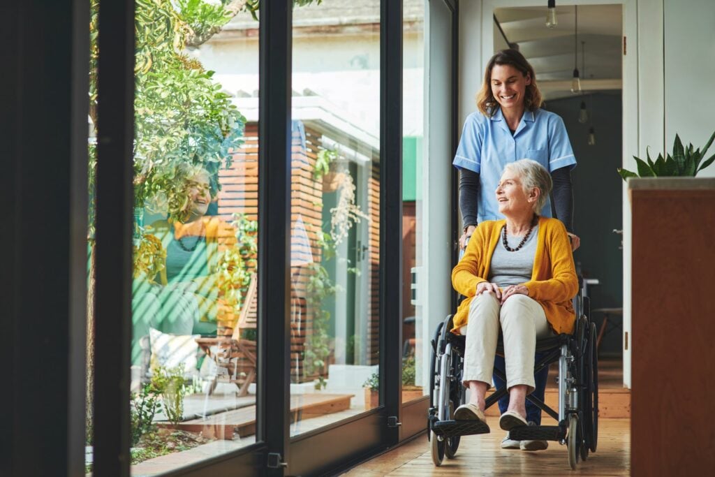 Young nurse pushing a senior woman in a wheelchair in an assisted living home.