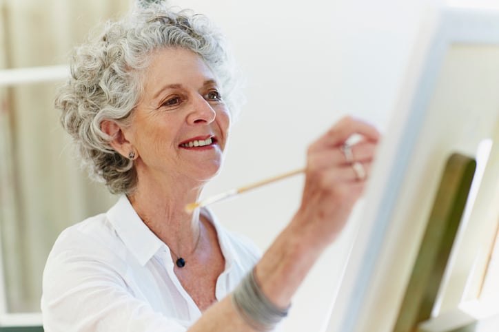 Senior woman smiling while painting on canvas