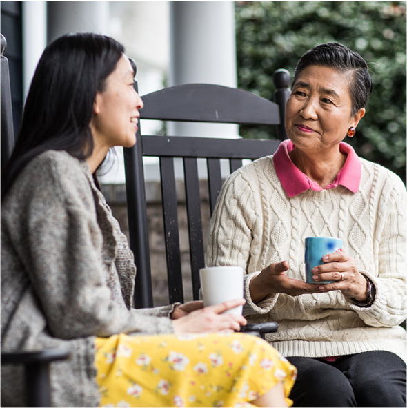 Senior woman and adult daughter having a conversation in rocking chairs on a front porch