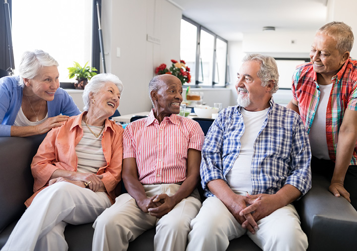 A group of 5 seniors gathered together on a couch laughing.