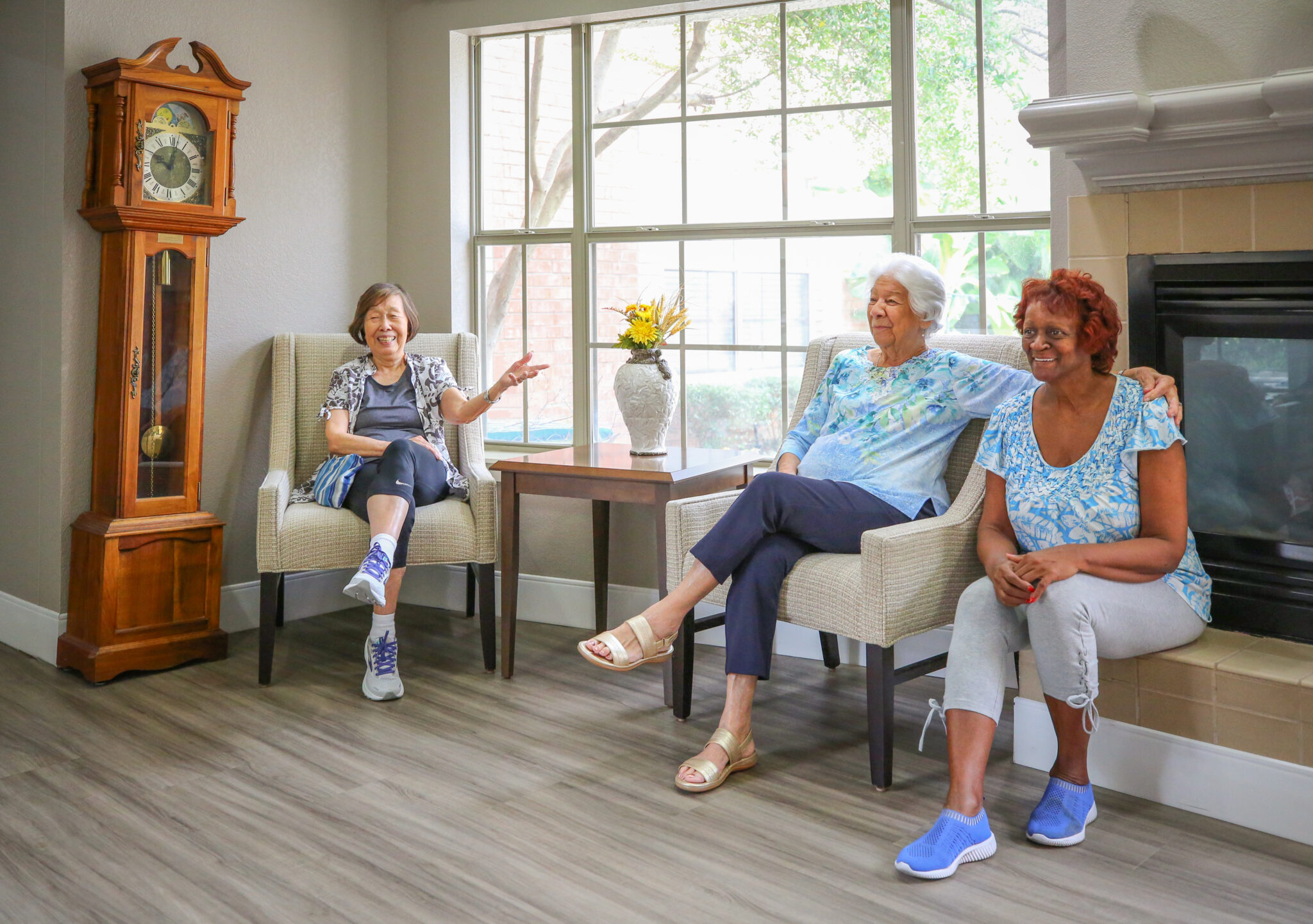 Three senior women enjoy conversation together by a fireplace
