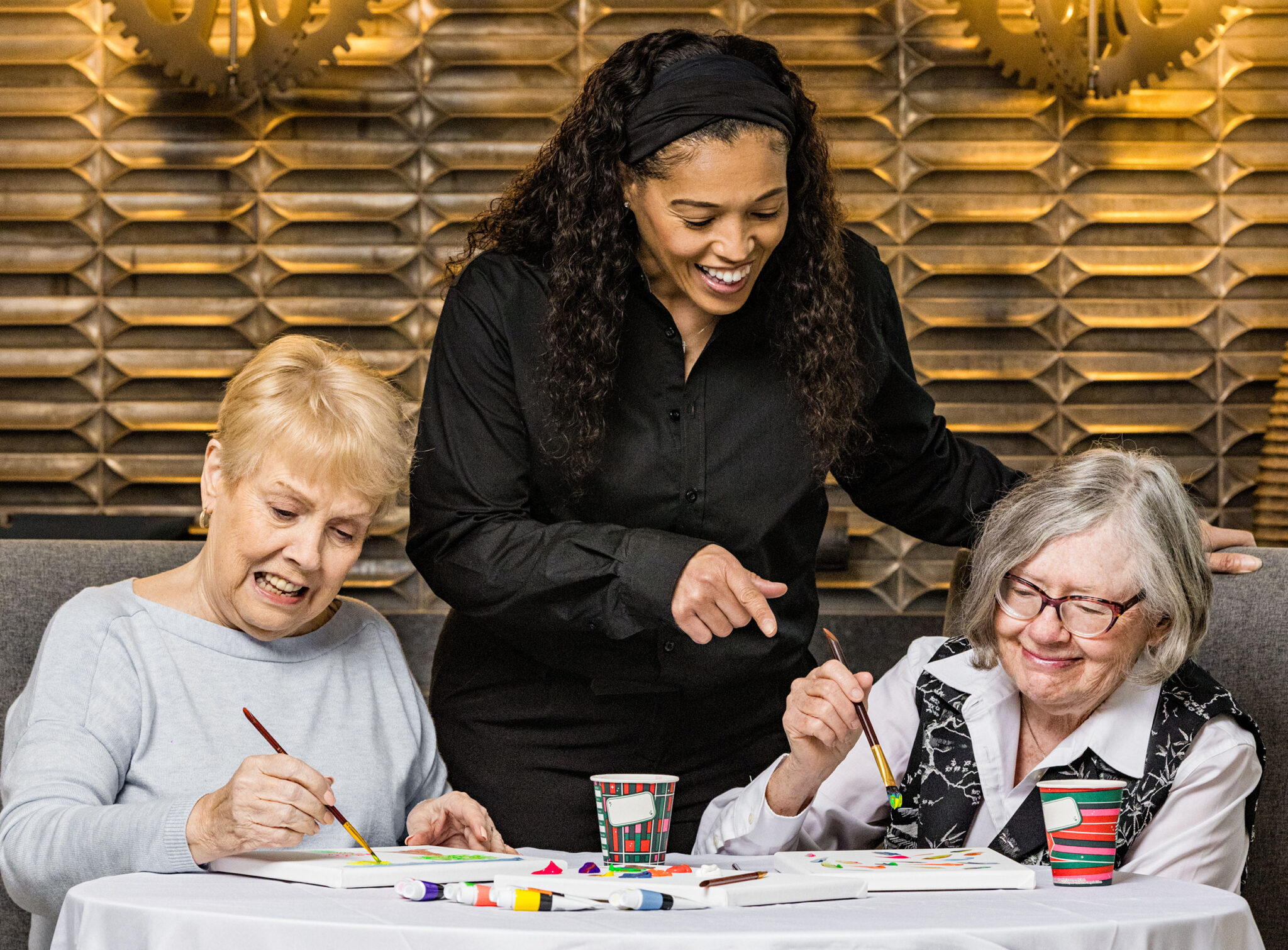 Two female residents paint together while a younger female caregiver admires their work