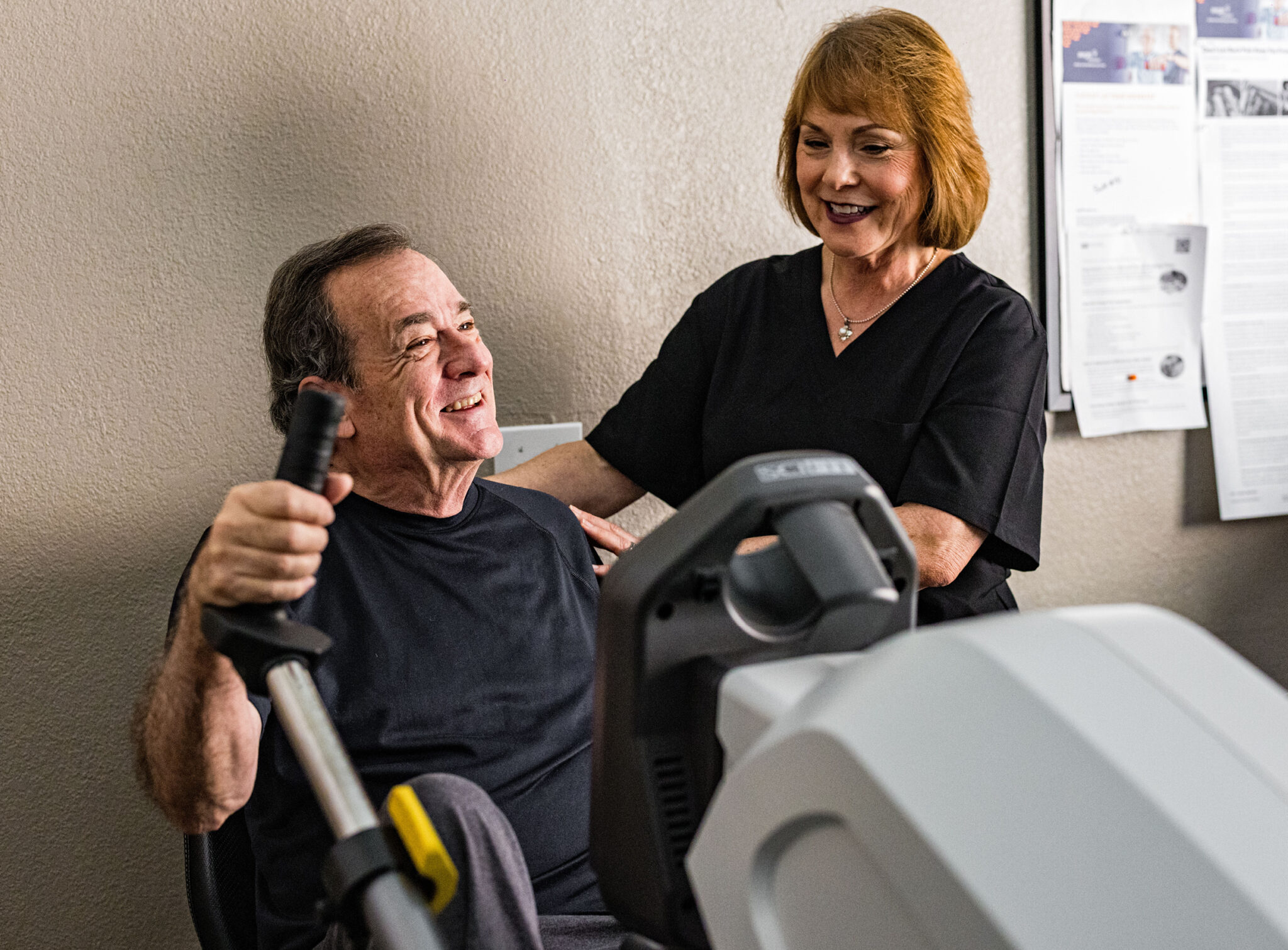 A female caregiver helps a male resident on exercise equipment