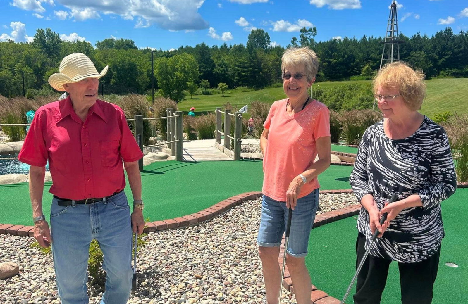 Three seniors smile while enjoying mini golf together outside