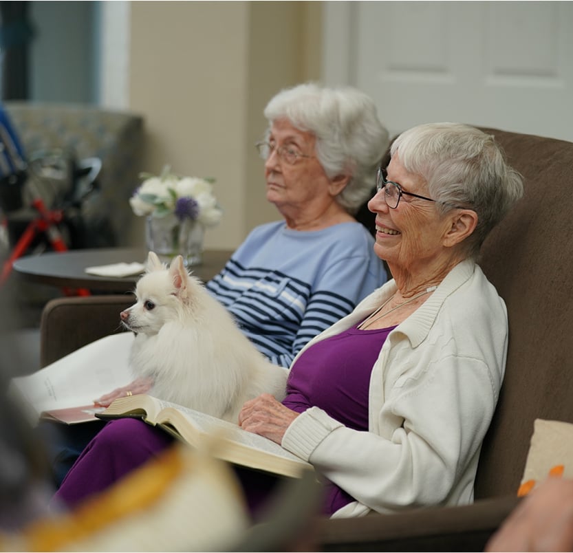 Two senior women on a couch with a small dog, enjoying all the benefits of a temporary stay
