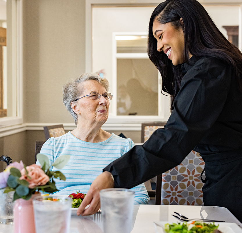 Senior at a community eating a salad brought to her by a caregiver