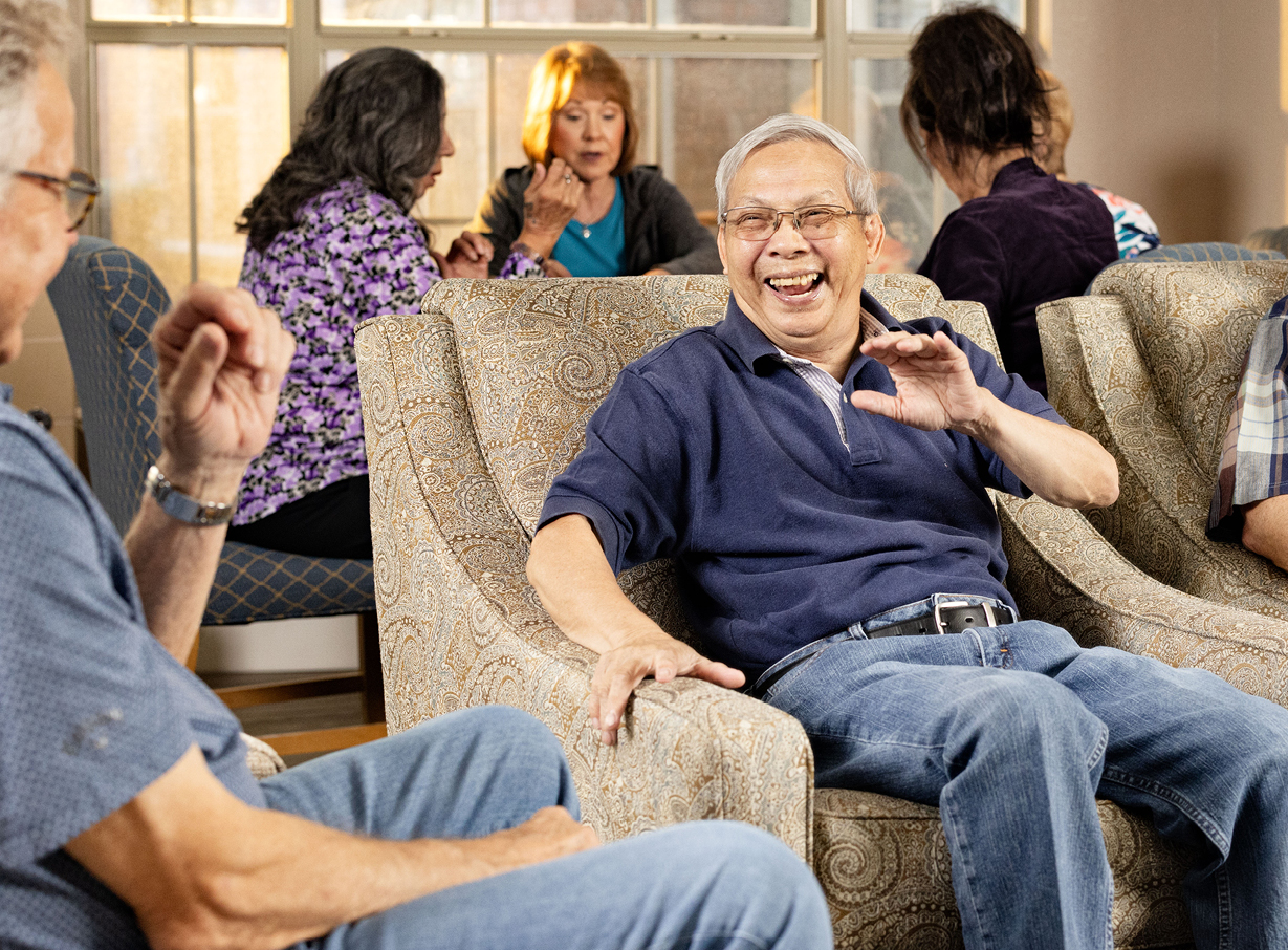 Two senior men sitting on chairs while talking to each other and laughing