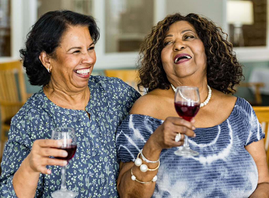 Two senior women laughing and drinking wine as they explore the benefits of independent living