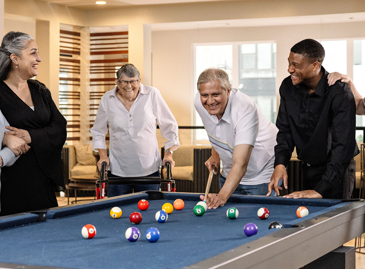 A group of seniors play billiards and laugh with caregivers
