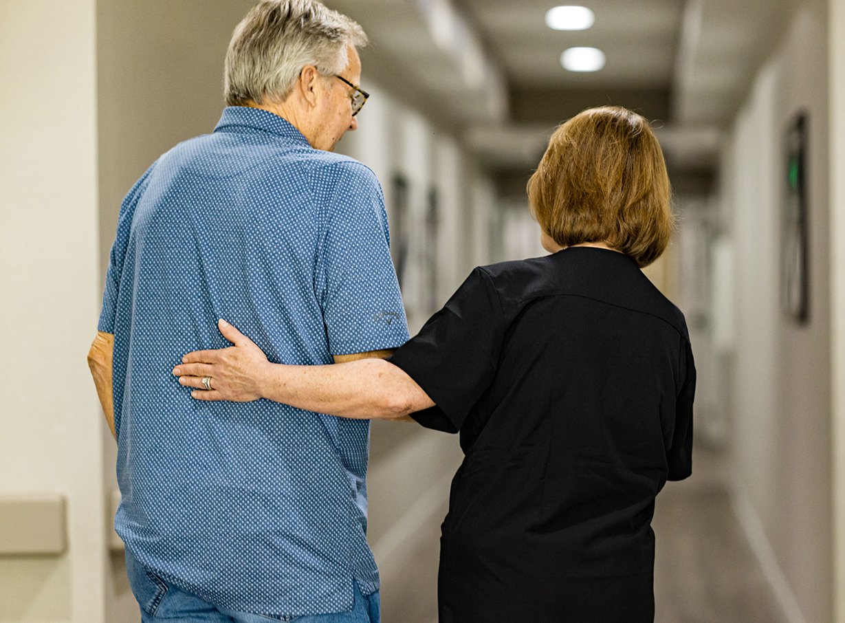 Senior man walking with his female caregiver, experiencing person-centered care at a senior living community