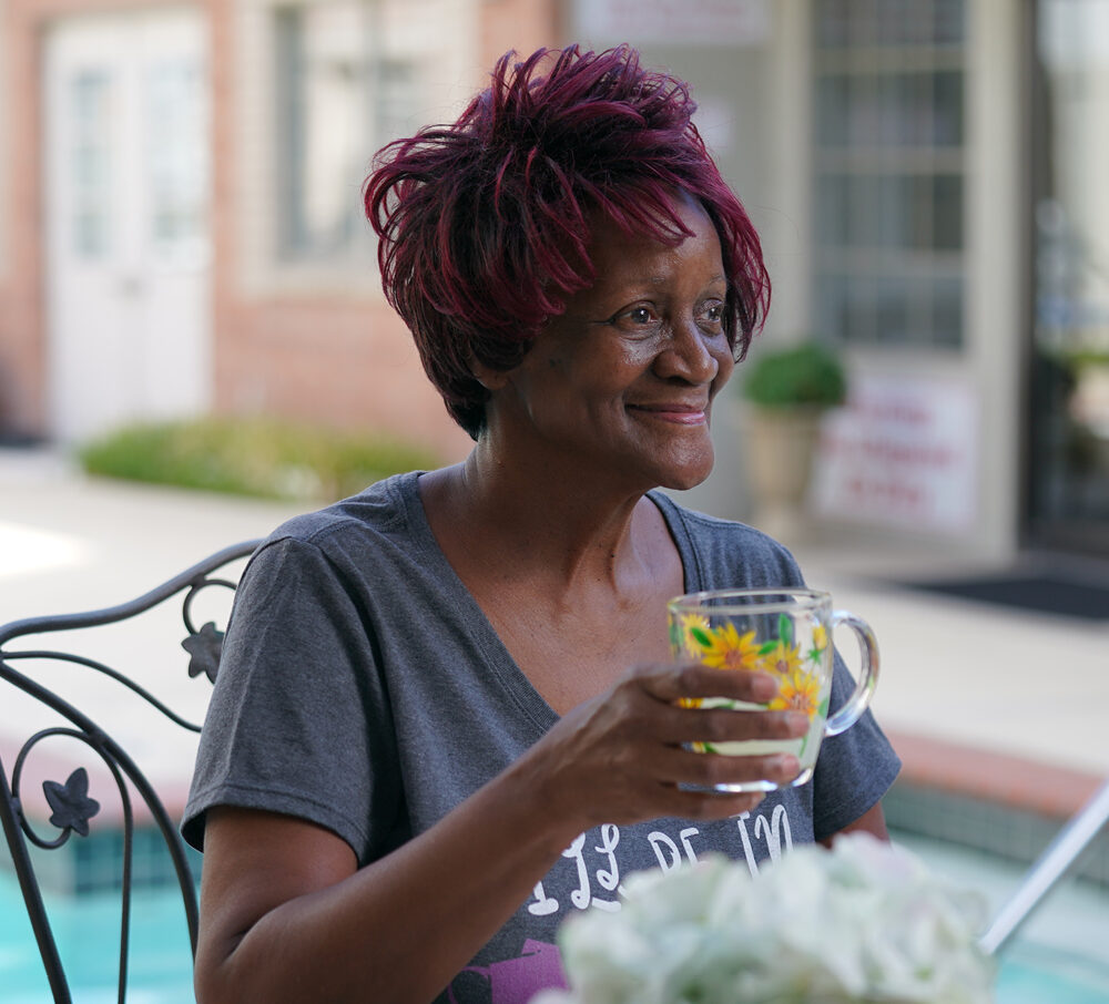 Senior woman holding a glass by a patio table outside discussing promises made in senior living