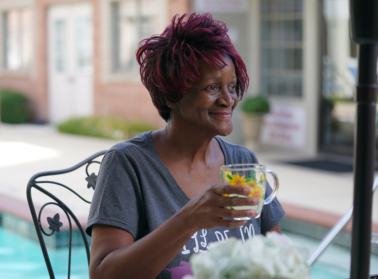 Senior woman holding a glass of lemonade while sitting outside by a pool at an independent living community