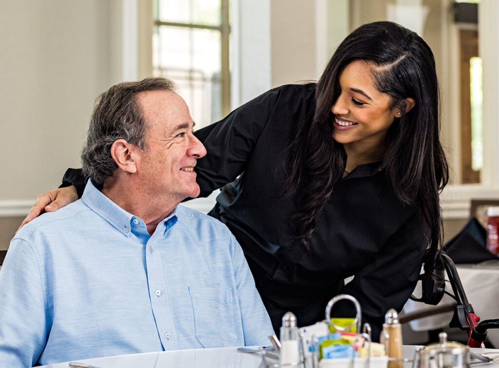 Caregiver helping a senior man sit at a restaurant table, our reason for caring