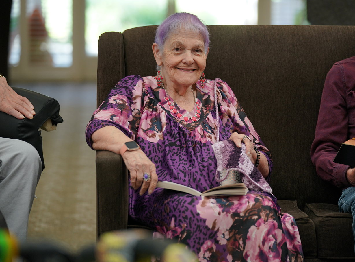 Senior woman sits and smiles on the couch while participating in Bible study in a senior living community