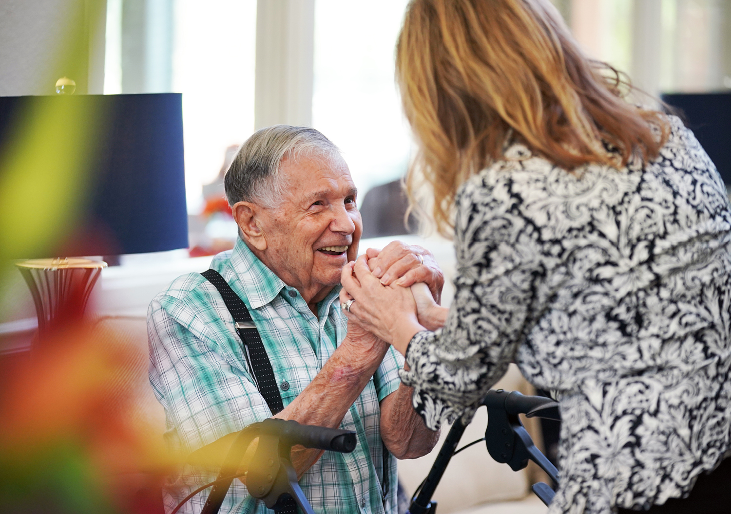 A senior man in an assisted living community holds hands with a female caregiver
