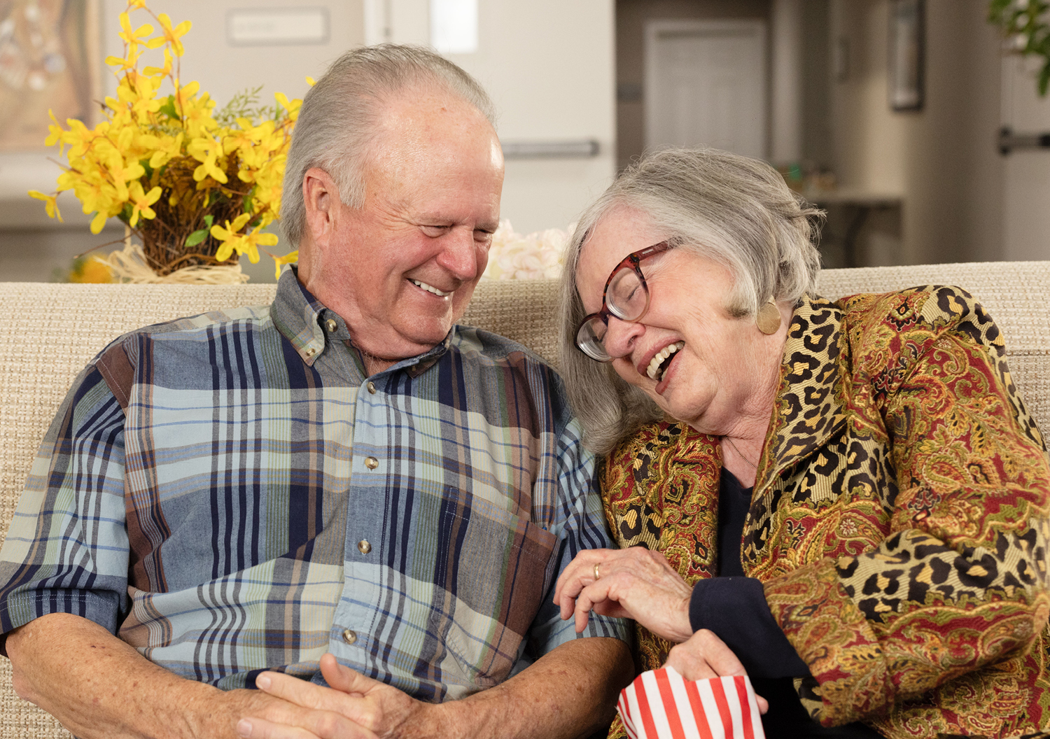 A senior couple, man and woman, laughing while eating popcorn and enjoying their independent living senior community