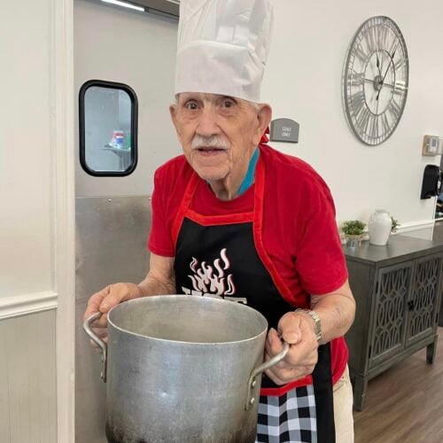 A senior man in a chef top hat holding a bowl