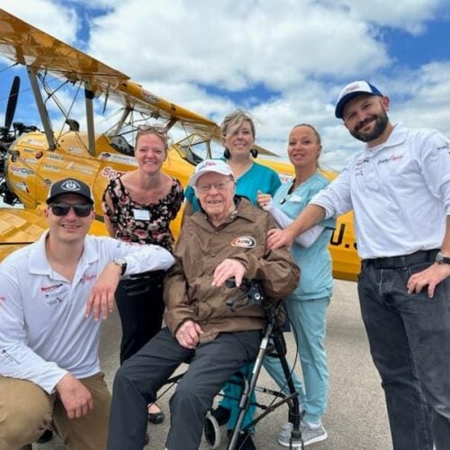 Four veteran senior men posing in front of a biplane