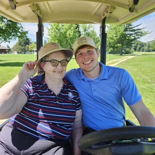 A senior woman and caregiver sitting in a golf cart posing after a round of golfing
