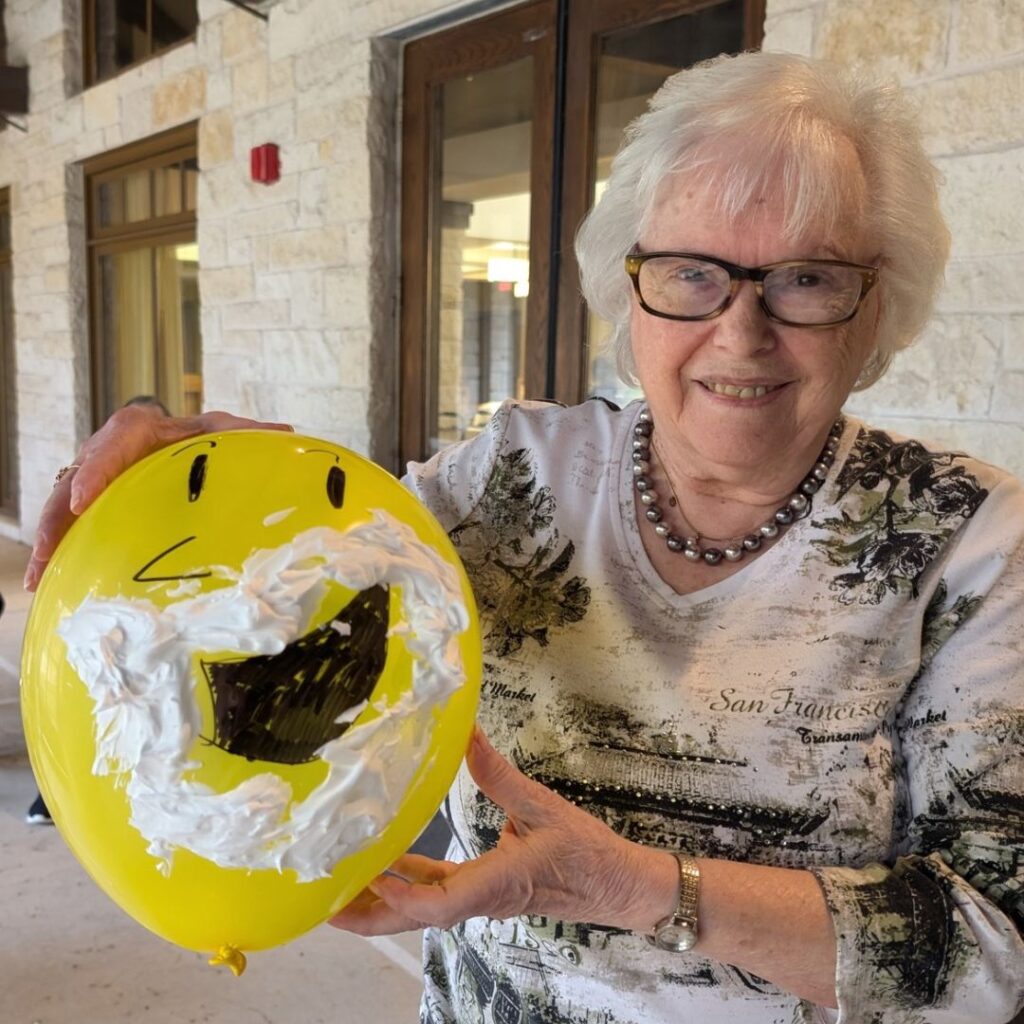 Woman holding a yellow balloon that has a face drawn on with a shaving cream beard