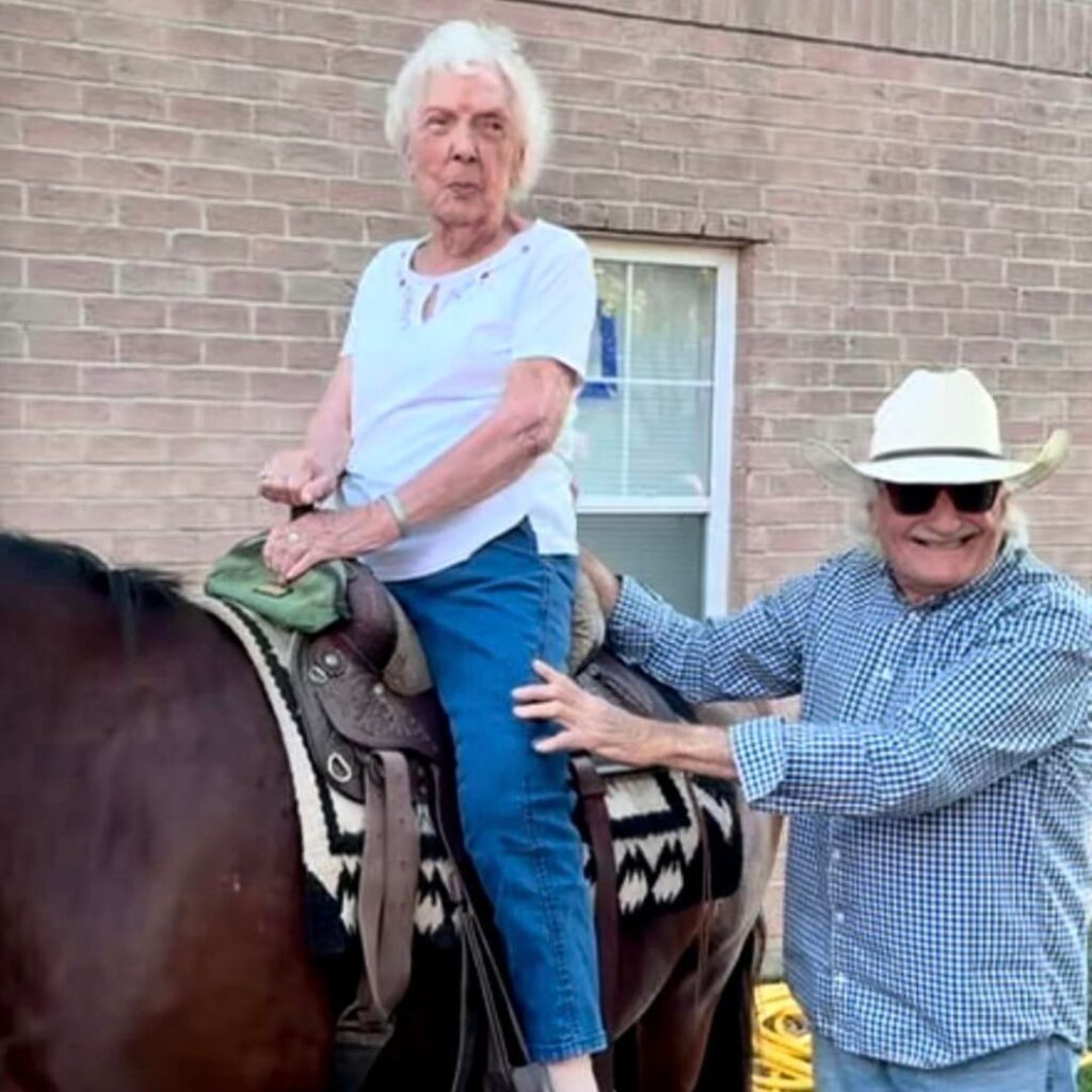 Woman sitting in the saddle of a brown horse with help from handler