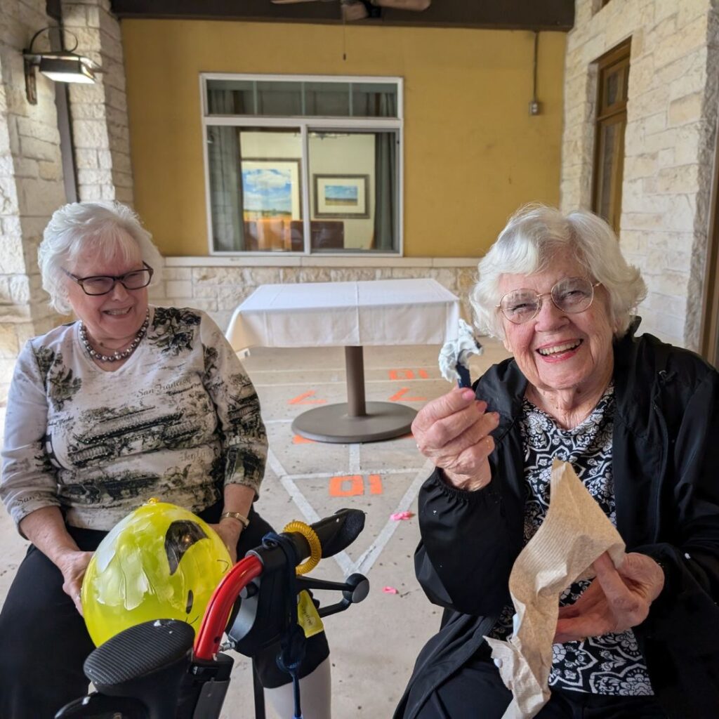 Two women laugh as one holds a yellow balloon and the other shows shaving cream fun