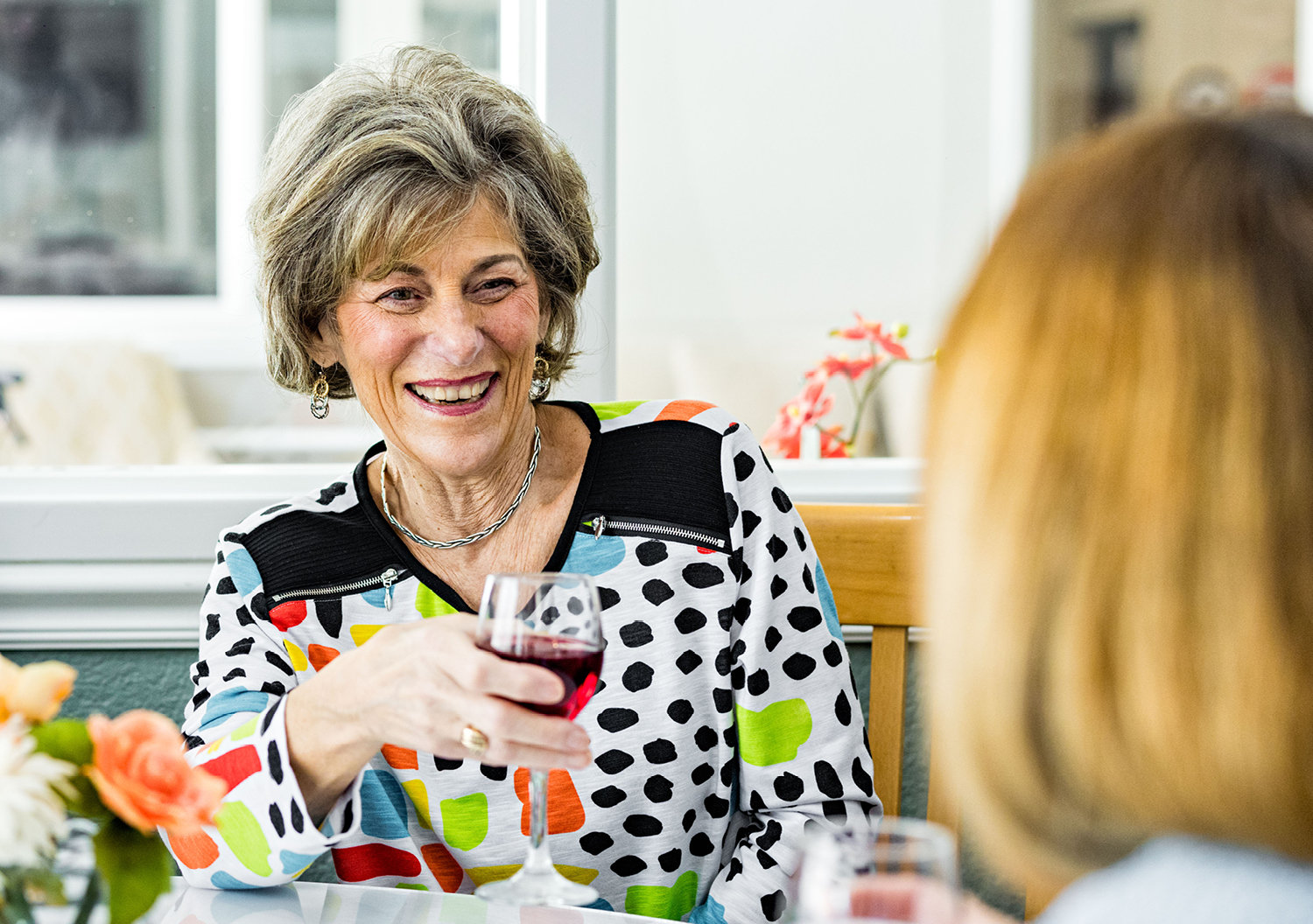 Senior woman drinking wine with another woman, smiling and laughing while discussing finding the right senior community