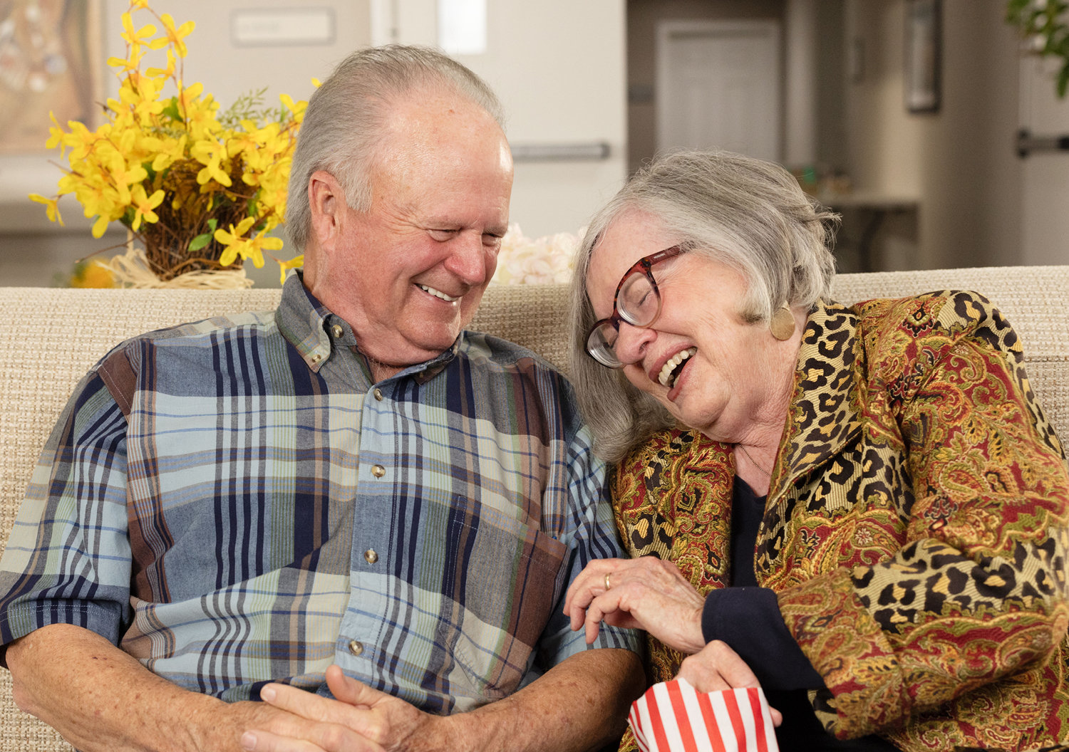 A senior couple, man and woman, laughing while eating popcorn and enjoying their Independant Living Senior Community