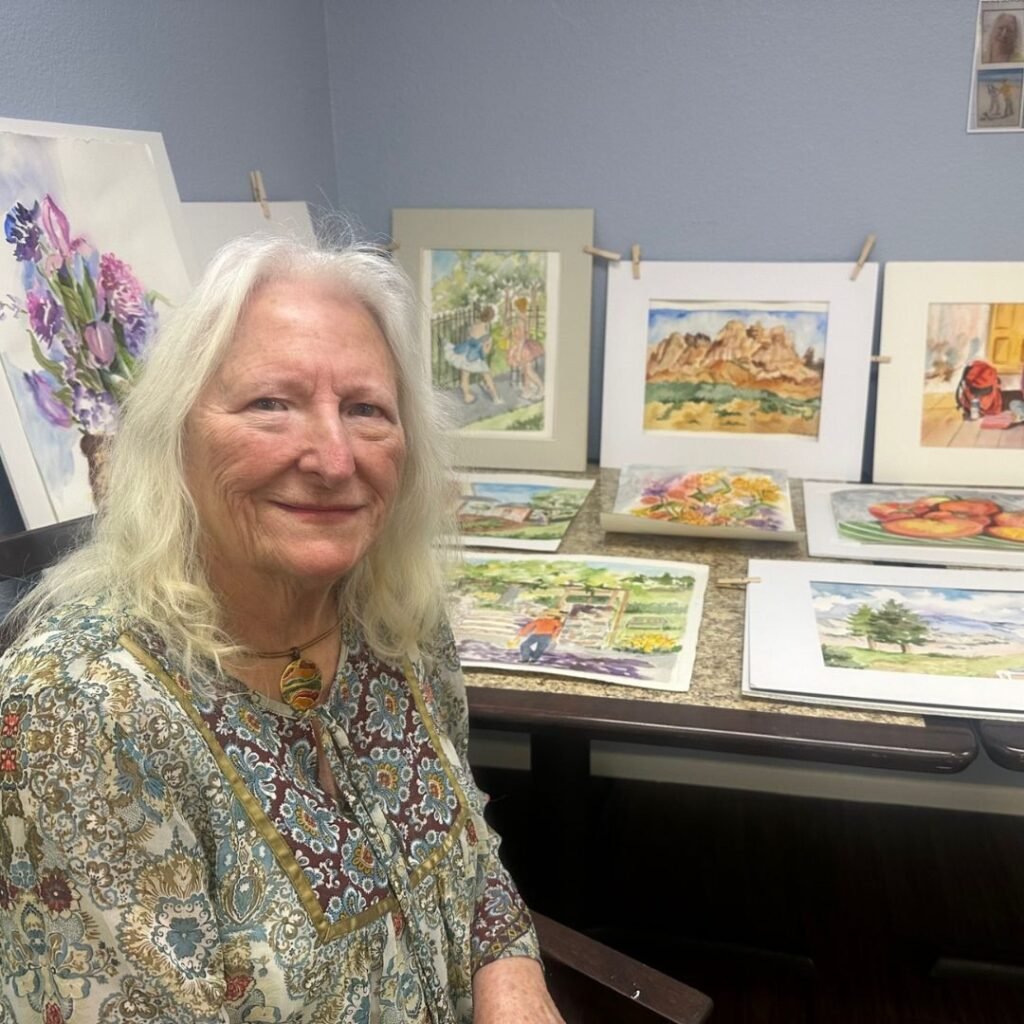 Resident painter sitting proudly in front of watercolor paintings