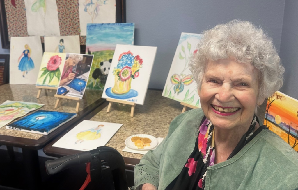 Resident painter sits proudly in front of her paintings