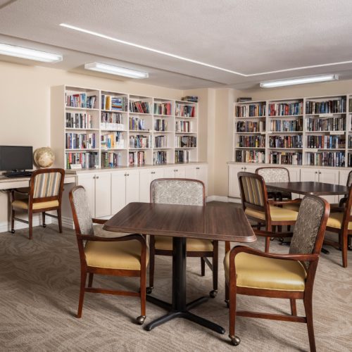 A library filled with bookshelves and books along with seating and a computer at a senior living community in Baytown, Texas