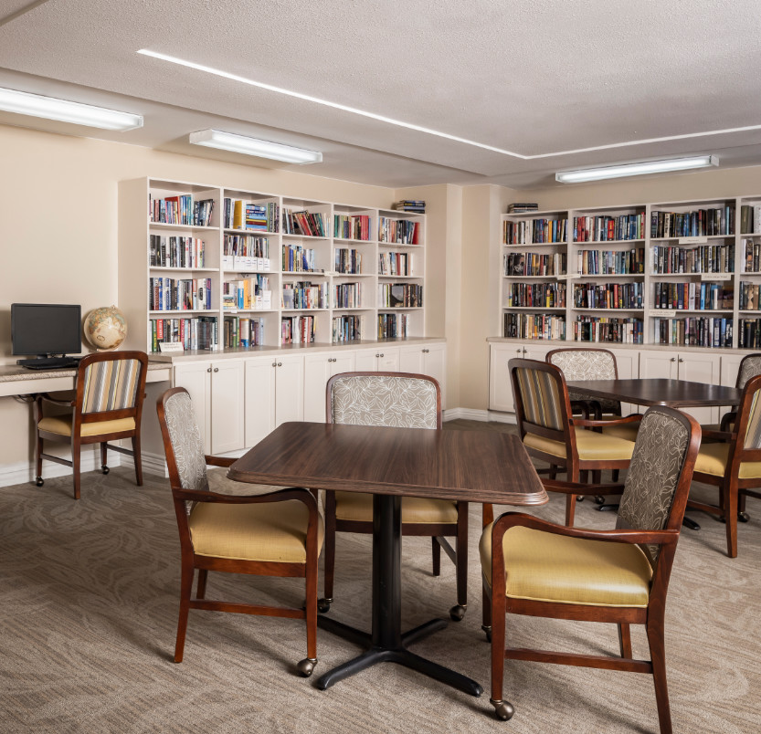 A library filled with bookshelves and books along with seating and a computer at a senior living community in Baytown, Texas