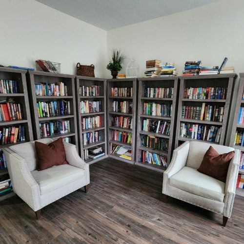 Multiple shelves of books and two chairs in a senior living community library