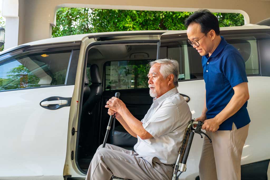 Elderly man with wheelchair being assisted into shuttle van
