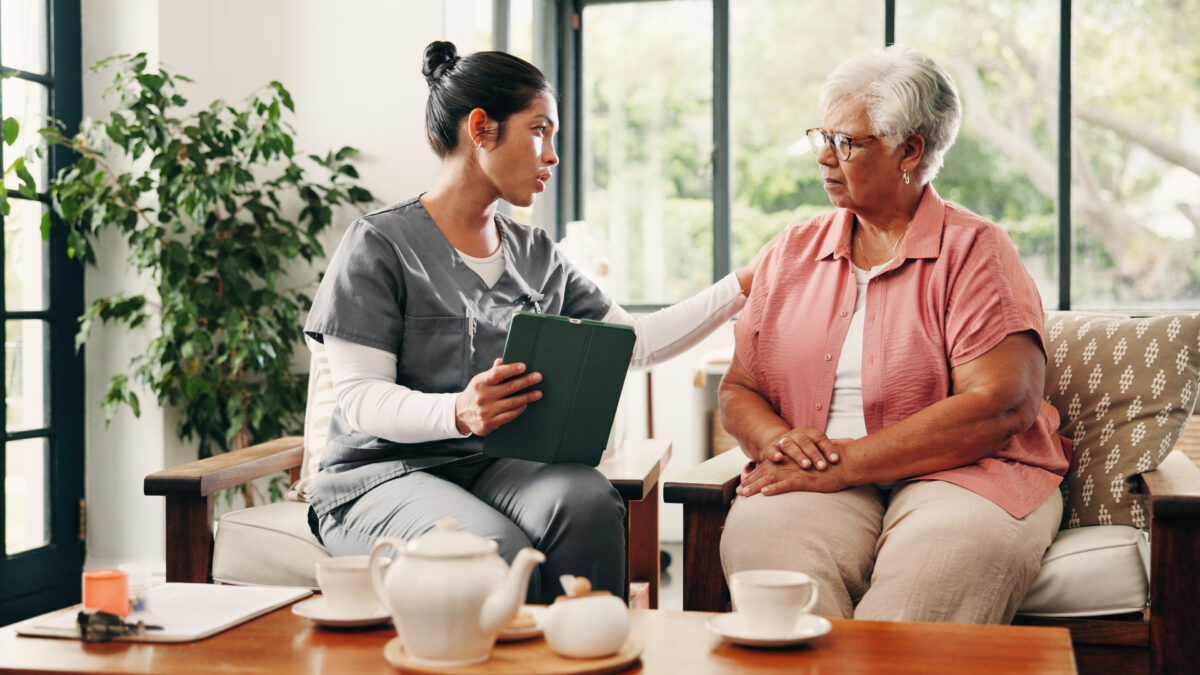 stock caregiver comforts senior woman on couch